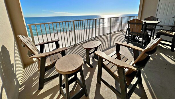 Ein Balkon mit Holzmöbeln, Blick auf den Strand und eine weiße Tür.