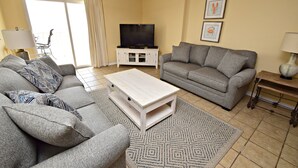 A living room with two grey sofas, a white coffee table, a TV on a white cabinet, and a patterned rug. - 🌞Make waves with a Beach Getaway!  Come enjoy the breeze! (Gulf Shores)