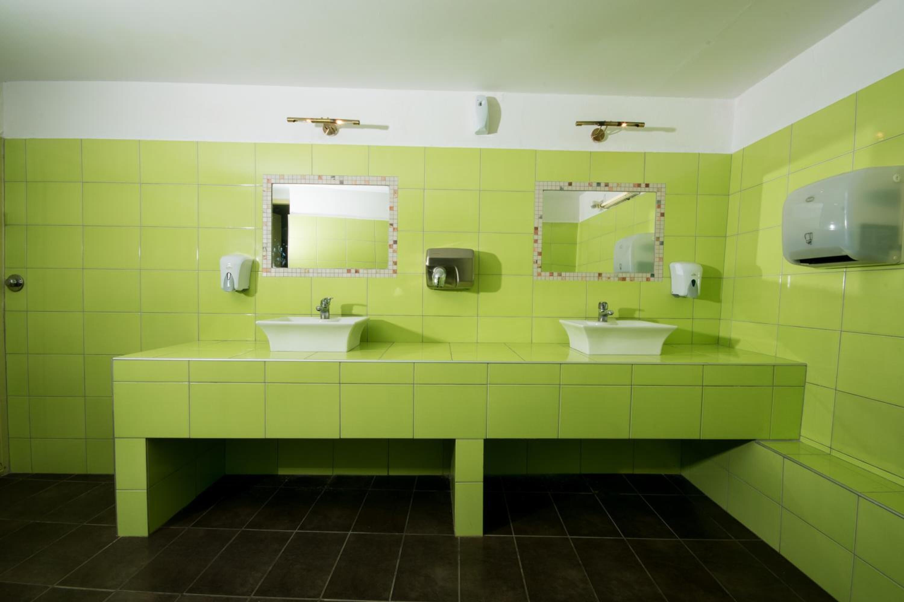 A bathroom with green tiles, two sinks, and two mirrors.