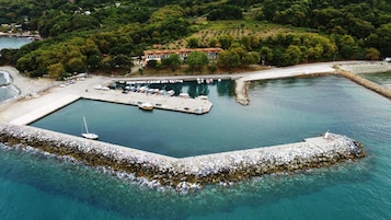 Vista aérea de una marina costera con un muelle, barcos y un edificio con techo rojo.
