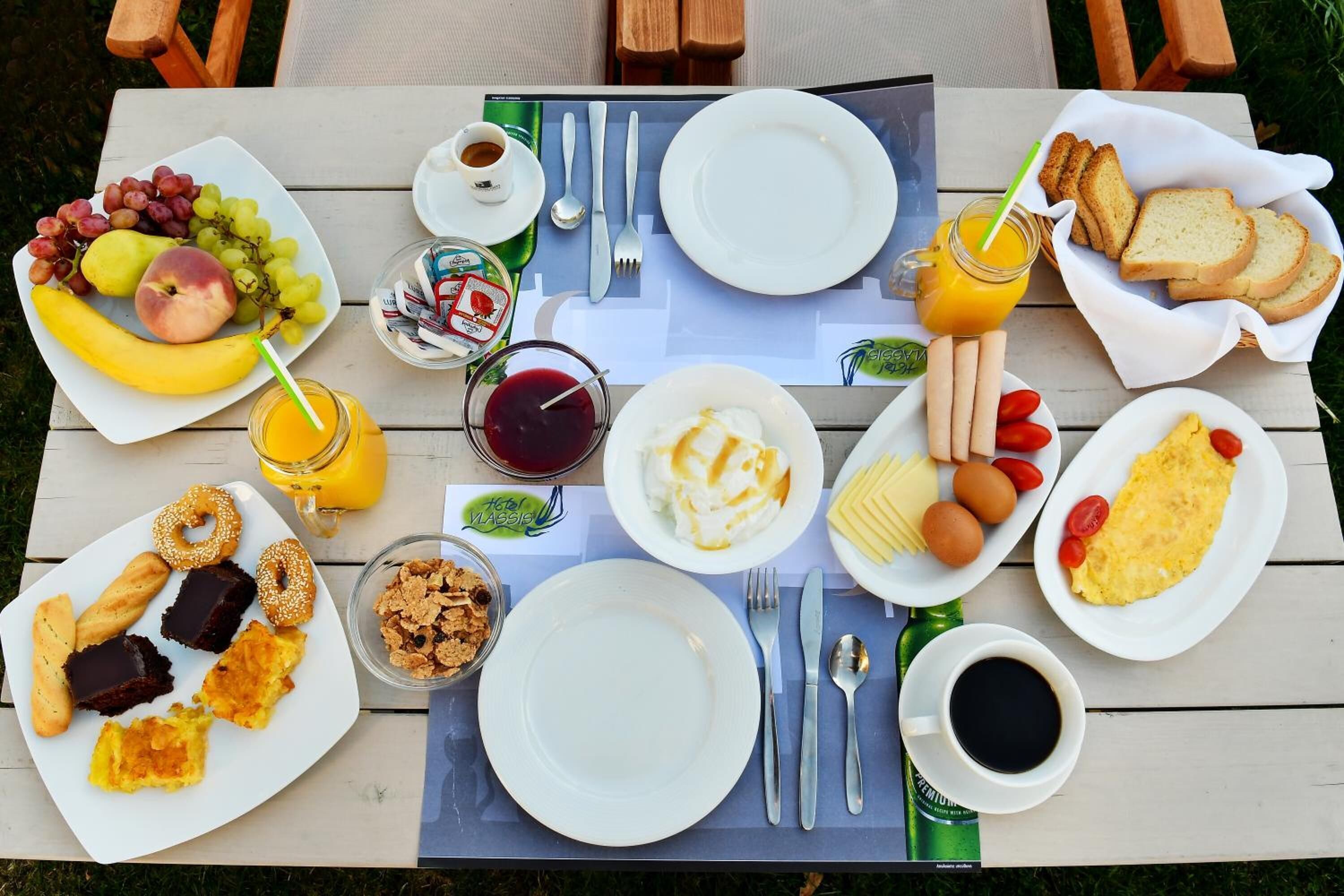 A table set with breakfast items including fruits, pastries, eggs, toast, and beverages.