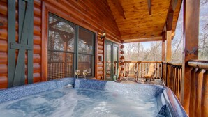 A wooden cabin with a hot tub on the porch, large windows, and a view of the surrounding forest. - Luxurious, Romantic, Cozy Cabin/Great Reviews/Close to Town/Clean/Hot tub! (Gatlinburg)
