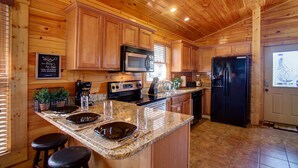 A kitchen with wooden cabinets, a granite countertop, a stainless steel refrigerator, and a microwave. - Luxurious, Romantic, Cozy Cabin/Great Reviews/Close to Town/Clean/Hot tub! (Gatlinburg)