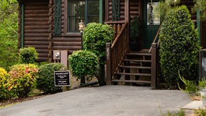 A rustic log cabin with a green door, a small porch, and a staircase leading to the entrance. - Luxurious, Romantic, Cozy Cabin/Great Reviews/Close to Town/Clean/Hot tub! (Gatlinburg)