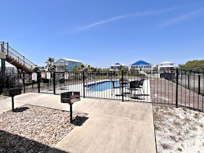 A pool area with a fence, a concrete walkway, and a few houses in the background.
