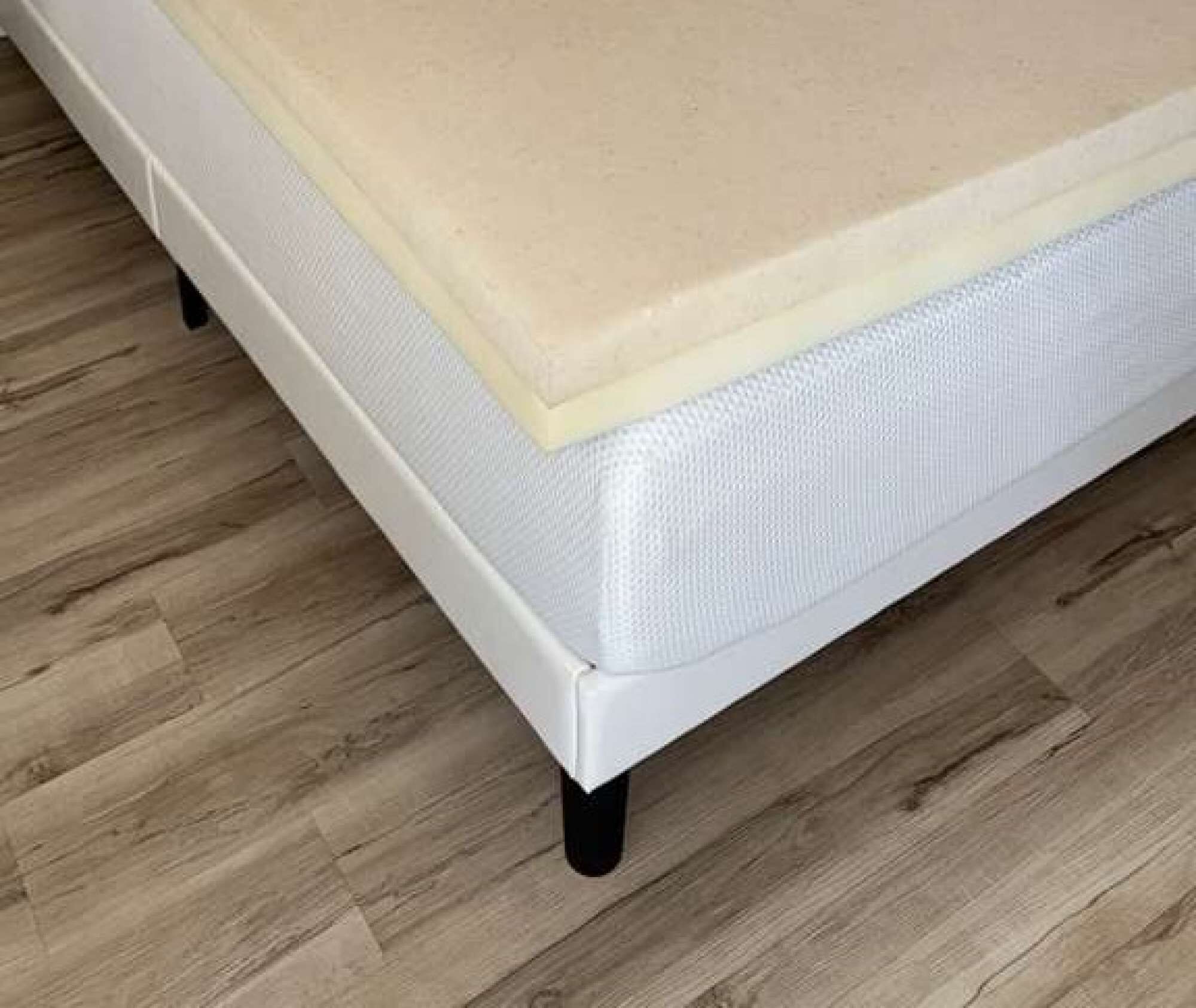 Una cama con colchón blanco y manta color beige, sobre un piso de madera.