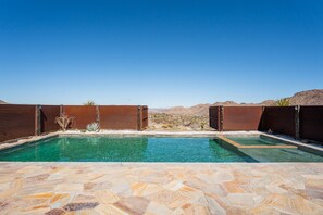 Piscina con terraza de piedra, rodeada de vallas de madera y paisaje desértico.