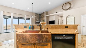 A kitchen with a built-in dishwasher, a stone countertop, and a view of the desert landscape.