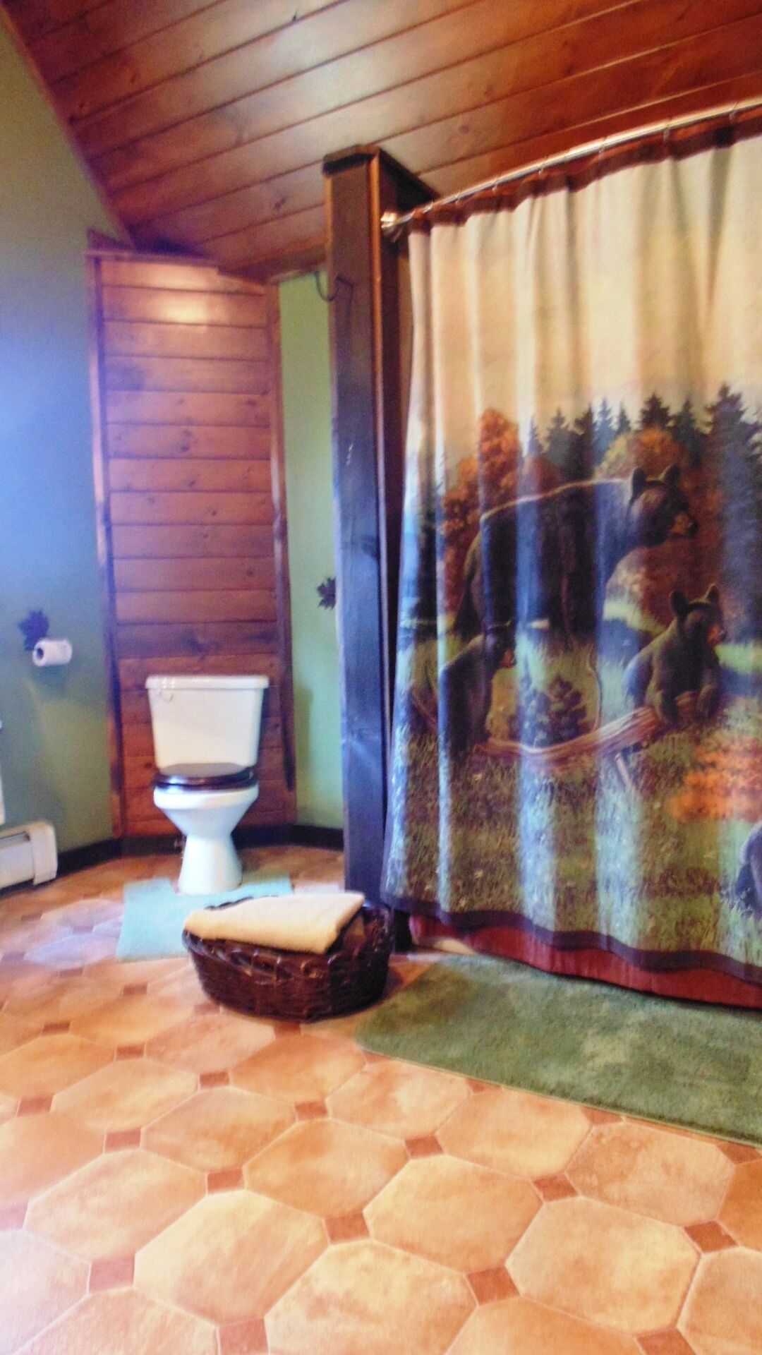 Een badkamer met houten vloer, toilet en een douchegordijn met een boslandschap.