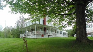 A large, two-story house with a porch and a large tree in front. - 70 Private Acres-SKI! SKI! SKI! (Athol)