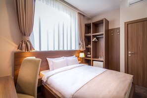 Ein Hotelzimmer mit Bett, Nachttisch mit Lampe, Kleiderschrank und Stuhl.