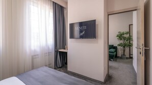 A hotel room with a bed, a desk, a chair, a potted plant, and a sign on the wall. - Veneti Suites (Belgrade)