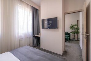 A hotel room with a bed, a desk, a chair, a potted plant, and a sign on the wall. - Veneti Suites (Belgrade)