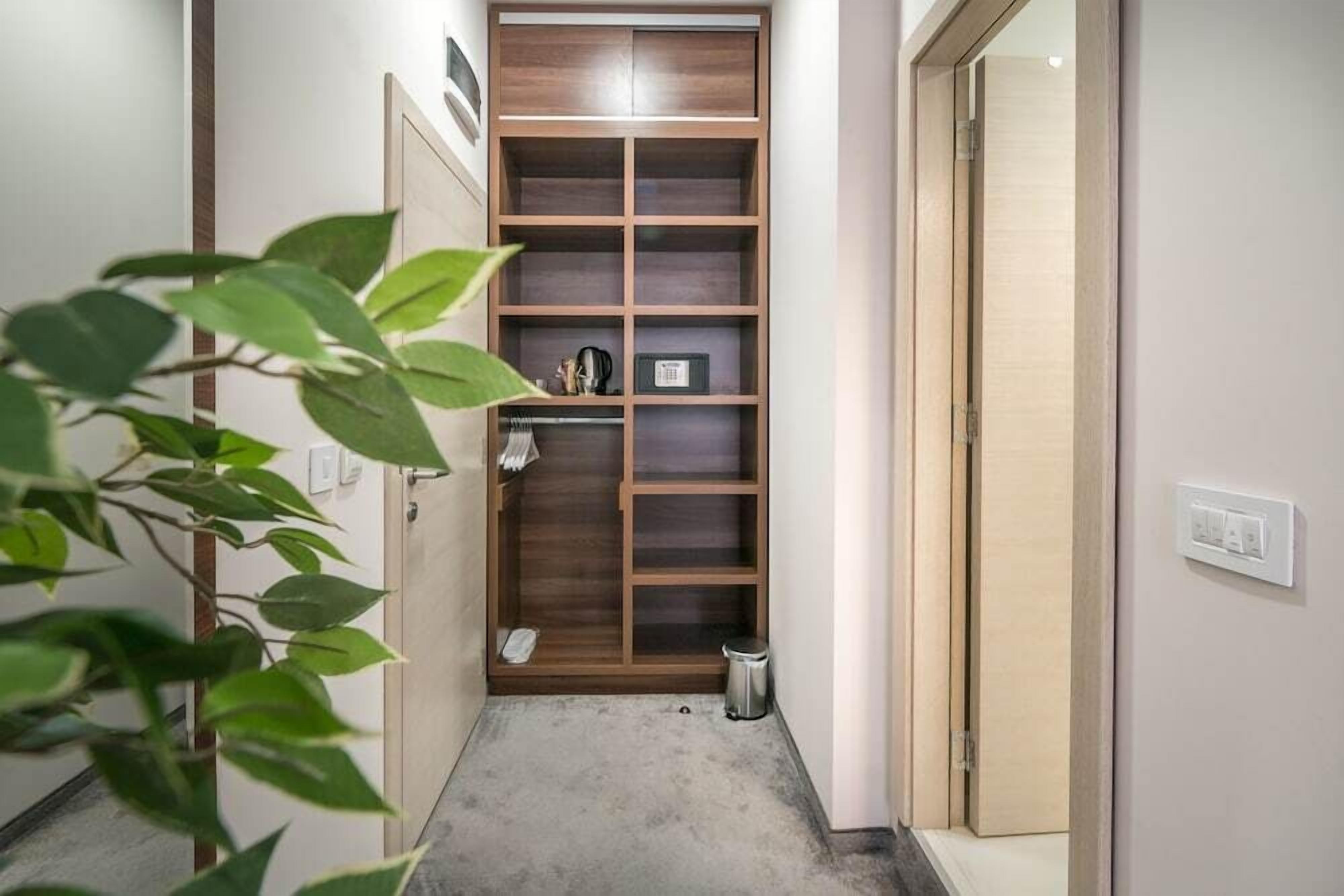 A narrow hallway with a wooden shelving unit, a trash bin, and a plant.