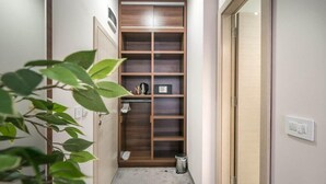 A narrow hallway with a wooden shelving unit, a trash bin, and a plant. - Veneti Suites (Belgrade)