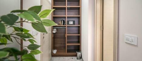 A narrow hallway with a wooden shelving unit, a trash bin, and a plant.
