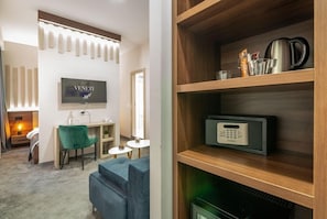 A modern hotel room with a flat-screen TV, a desk with a chair, a sofa, a wooden shelf with a kettle and a coffee maker, and a thermostat. - Veneti Suites (Belgrade)
