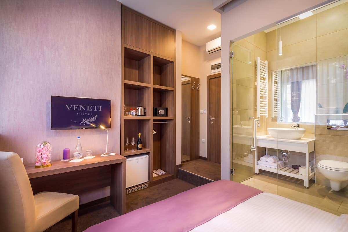 A hotel room with a bed, desk, wardrobe, and a bathroom with a sink and mirror.
