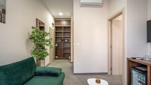 A compact living space with a green sofa, a small white table, a potted plant, a built-in TV, and a wooden cabinet. - Veneti Suites (Belgrade)