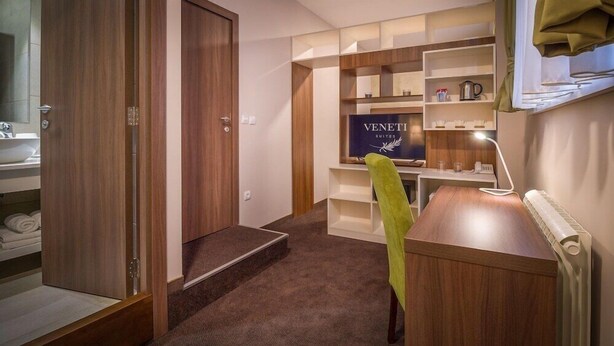 A hotel room with a wooden desk, a chair, a radiator, and a shelf with toiletries. - Veneti Suites (Belgrade)
