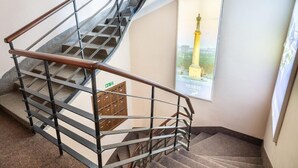 A staircase with metal railings and carpeted steps, leading to a landing with a wooden door and a poster of a monument. - Veneti Suites (Belgrade)