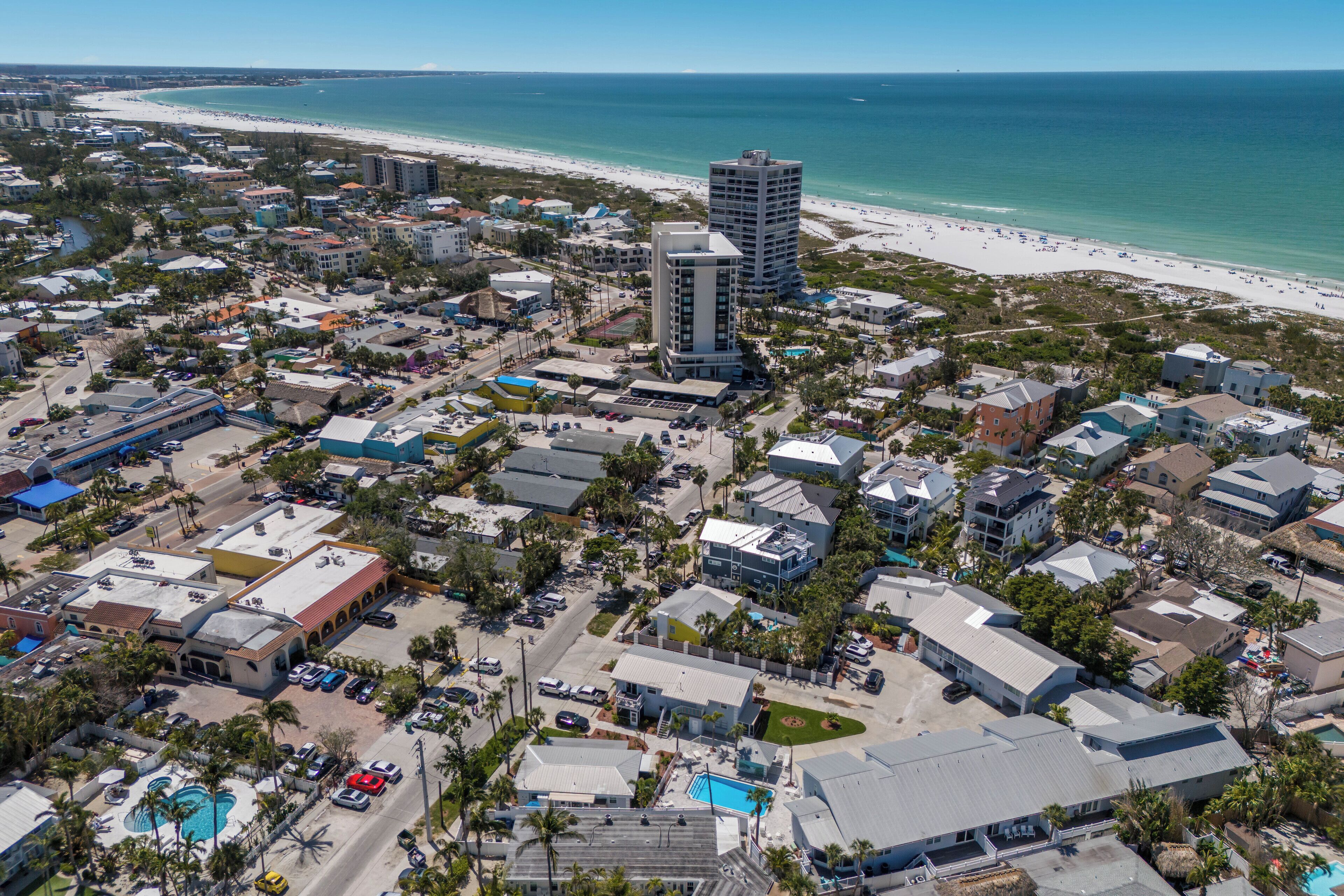 Vista aérea de un pueblo costero con playa, edificios y piscina.