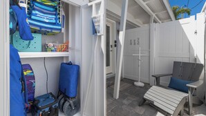 A compact outdoor seating area with a chair and a small table, a storage unit with various items, and a white door leading to another room. - Perfect Local In Village,1 1/2 Block From #1 Beach In USA, Pool, Wifi, Sun & Fun (Siesta Key)