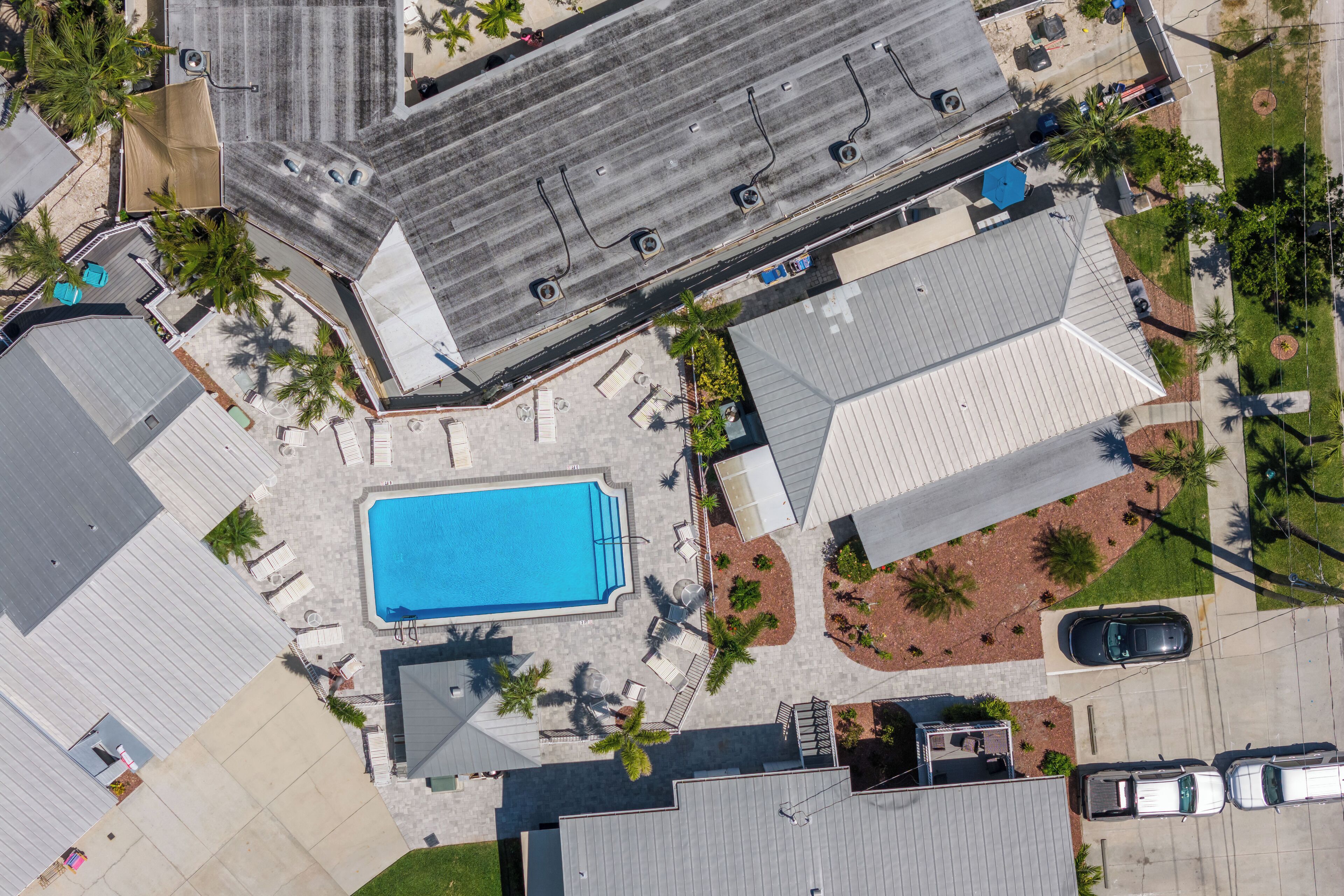 An aerial view of a residential area with a swimming pool, multiple cars, and a few palm trees.