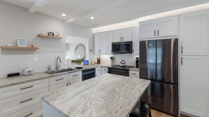 A modern kitchen with white cabinetry, a stainless steel refrigerator, and a marble countertop. - Perfect Local In Village,1 1/2 Block From #1 Beach In USA, Pool, Wifi, Sun & Fun (Siesta Key)
