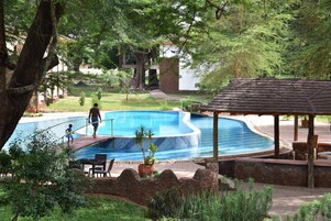 A swimming pool with a wooden deck, surrounded by greenery and a gazebo.