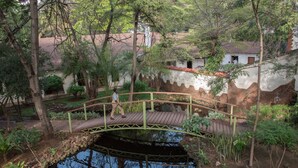 A wooden bridge over a pond with a stone wall and trees in the background. - Hunters Lodge - Kiboko (Kiboko)