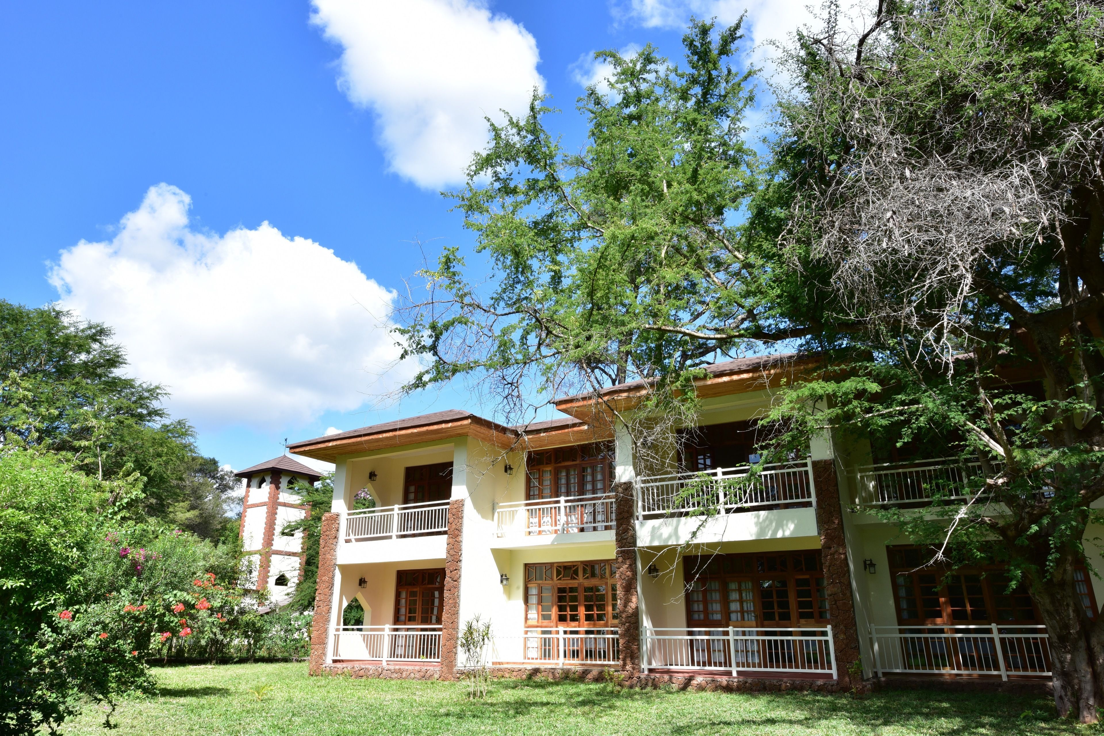 A two-story building with balconies, surrounded by lush greenery and a clear sky.