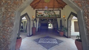 A stone-walled lobby with a wooden ceiling, a large mural, and potted plants. - Hunters Lodge - Kiboko (Kiboko)