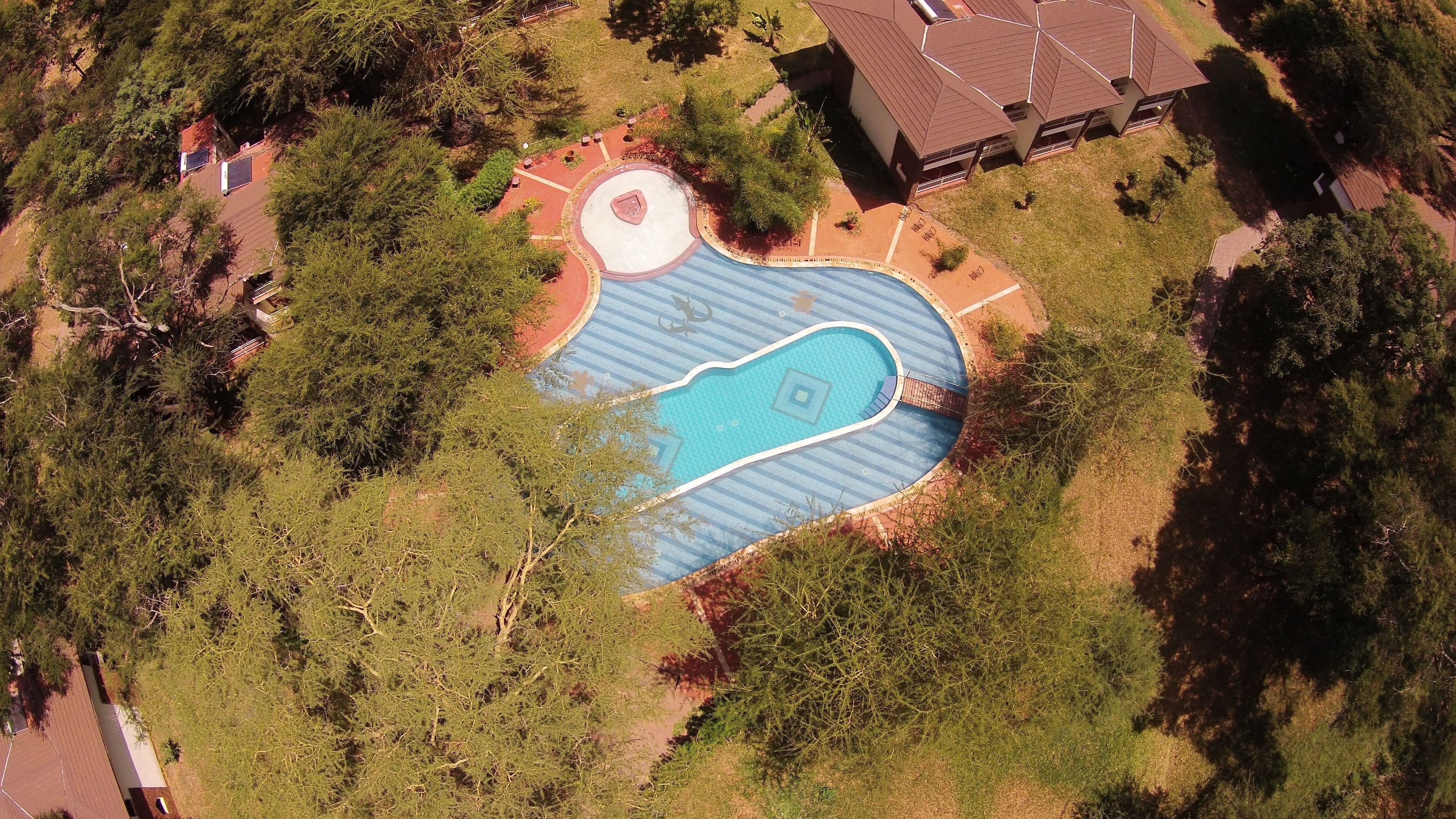 An aerial view of a residential area with a swimming pool, a tennis court, and a building with a unique roof design.