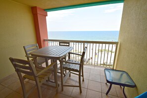 Uma varanda com mesa e cadeiras, uma mesinha pequena e vista para o oceano.