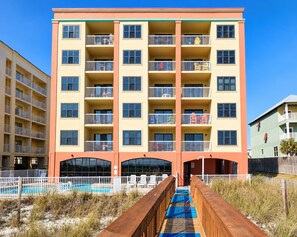 A multi-story hotel with balconies, a swimming pool, and a wooden deck leading to the entrance.