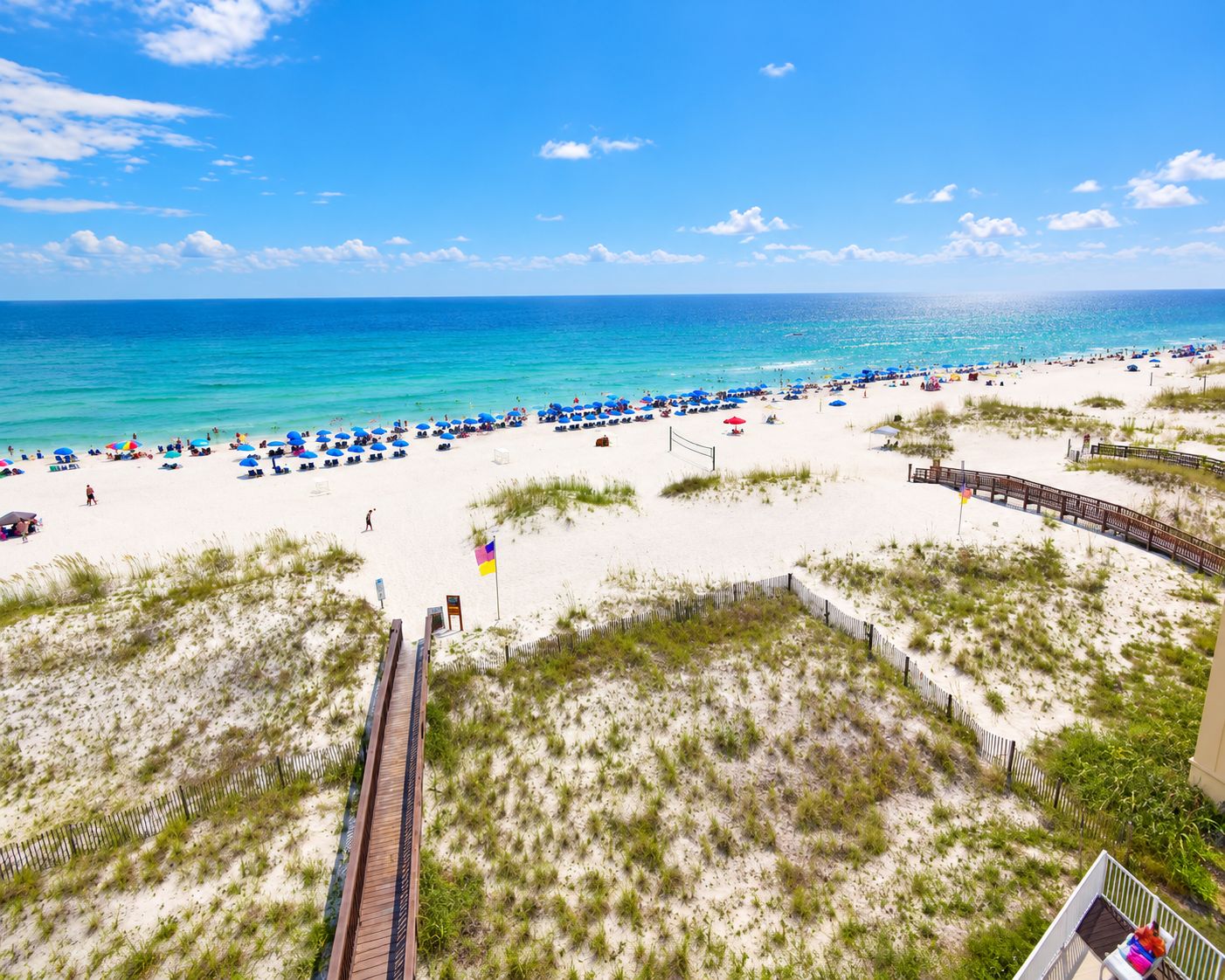 A beach with a wooden boardwalk, beach umbrellas, and a clear view of the ocean.