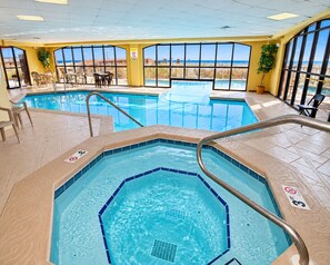 An indoor swimming pool with a view of the beach, surrounded by yellow walls and large windows.