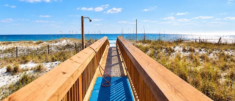 A wooden boardwalk leading to a beach with a clear sky.