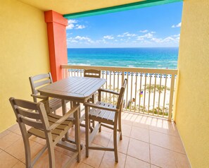 A balcony with a table and chairs, overlooking a beach with a clear view of the ocean.