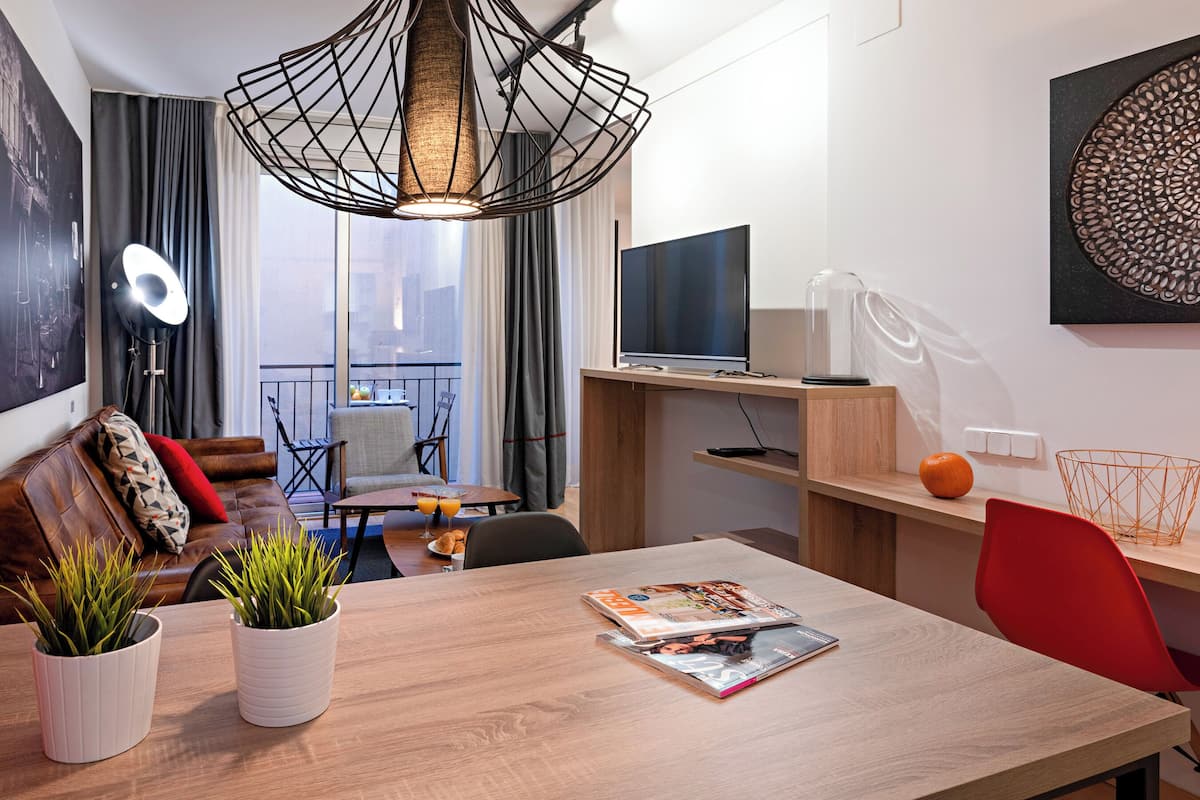 Ein modernes Wohnzimmer mit einem Holzesstisch, einem roten Sessel und einem Fernseher auf einem Holzboden. Auf dem Tisch stehen zwei Blumentöpfe und es gibt ein großes Fenster mit Vorhängen.