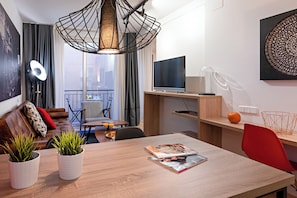A modern living room with a dining area, a television, and a balcony with a view. - Habitat Apartments Hot Jazz (Barcelona)