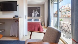 A hotel room with a bed, a chair, a TV, and a balcony with a view of buildings. - Habitat Apartments Hot Jazz (Barcelona)
