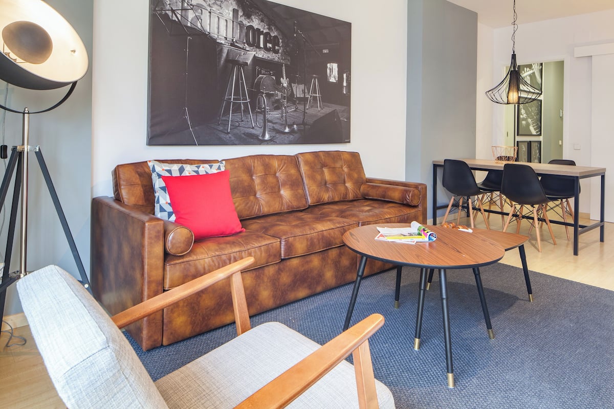 Ein modernes Wohnzimmer mit einem braunen Ledersofa, einem runden Couchtisch und einem Essbereich mit Holztisch und Stühlen.