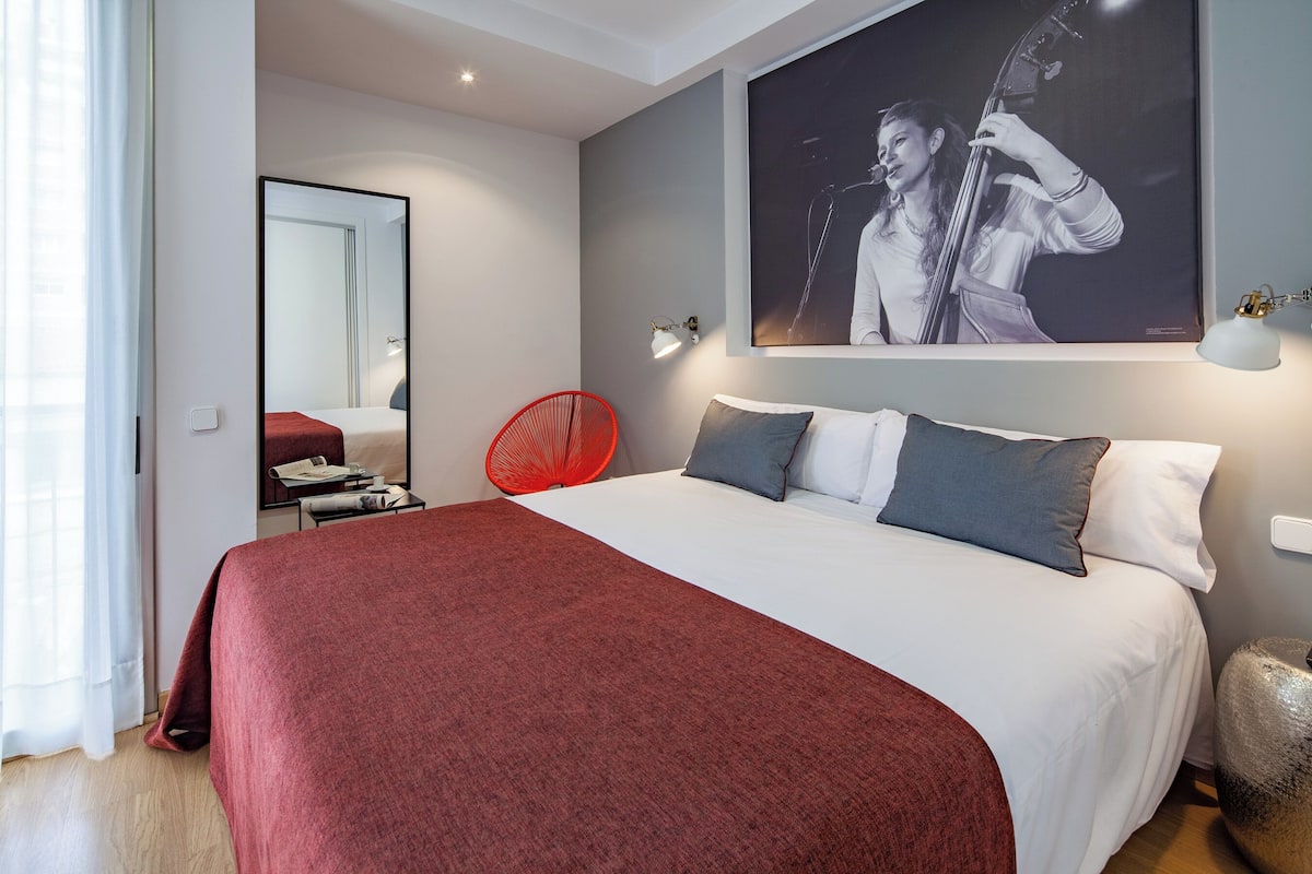 Ein modernes Hotelzimmer mit einem großen Bett, einem roten Sessel, einem Wandbild eines Musikers und einem Nachttisch mit einer Lampe.