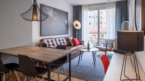 A modern living room with a wooden dining table, leather sofa, and a large window with curtains. - Habitat Apartments Hot Jazz (Barcelona)