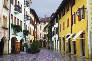 Una calle estrecha flanqueada por edificios, con balcones, toldos y un camino de adoquines.