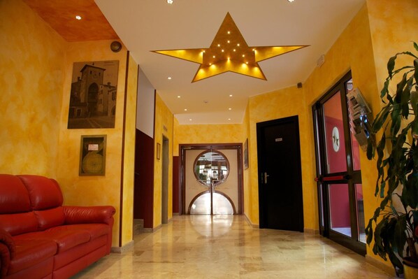 Un vestíbulo de hotel con una lámpara de techo en forma de estrella, un sofá de cuero rojo, una puerta de cristal de entrada y un cuadro en la pared.