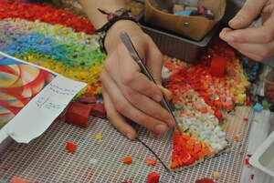 Manos cortando cubos de plástico de colores sobre una superficie de malla.