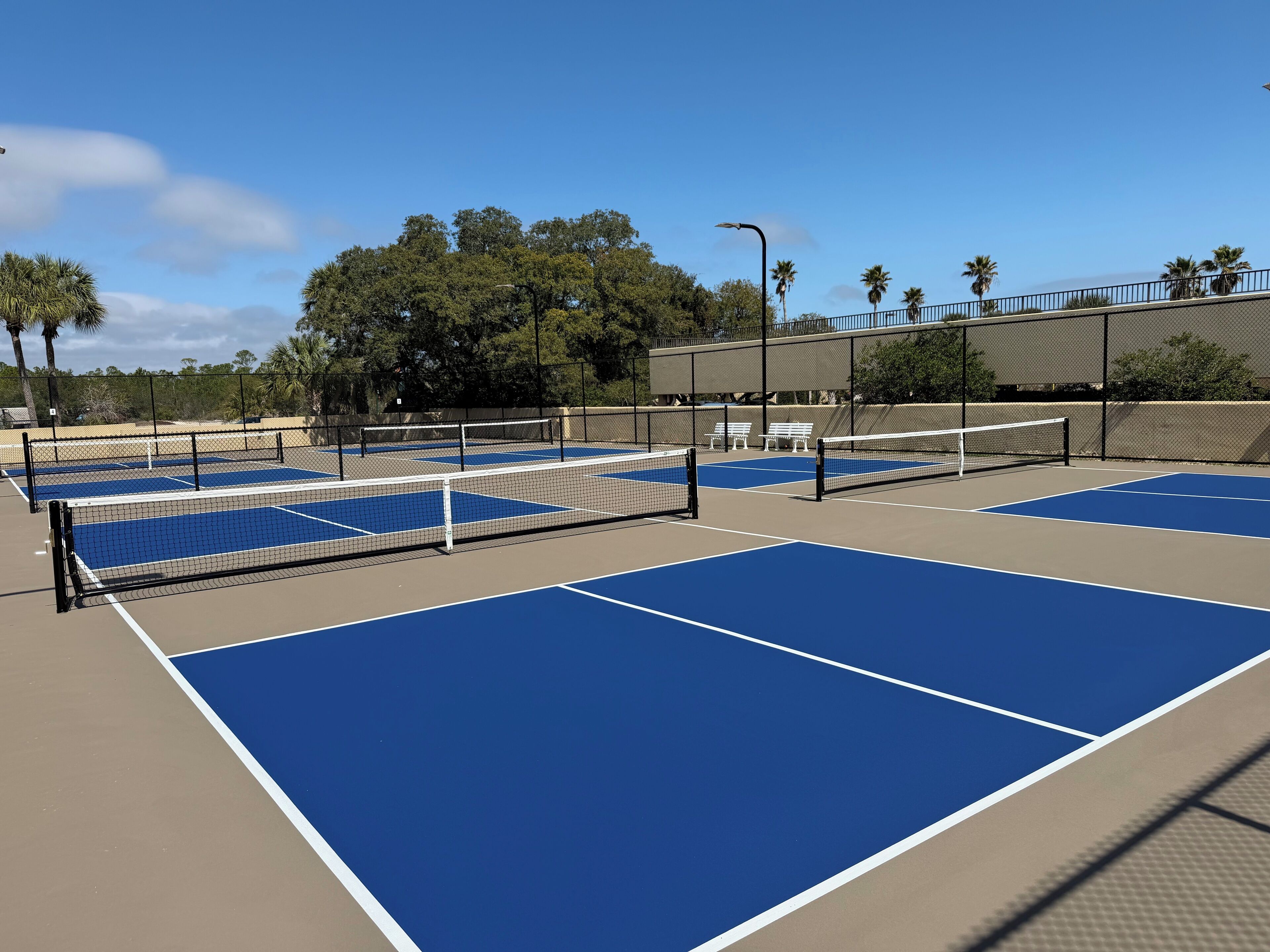 A tennis court with multiple courts, benches, and a fence.